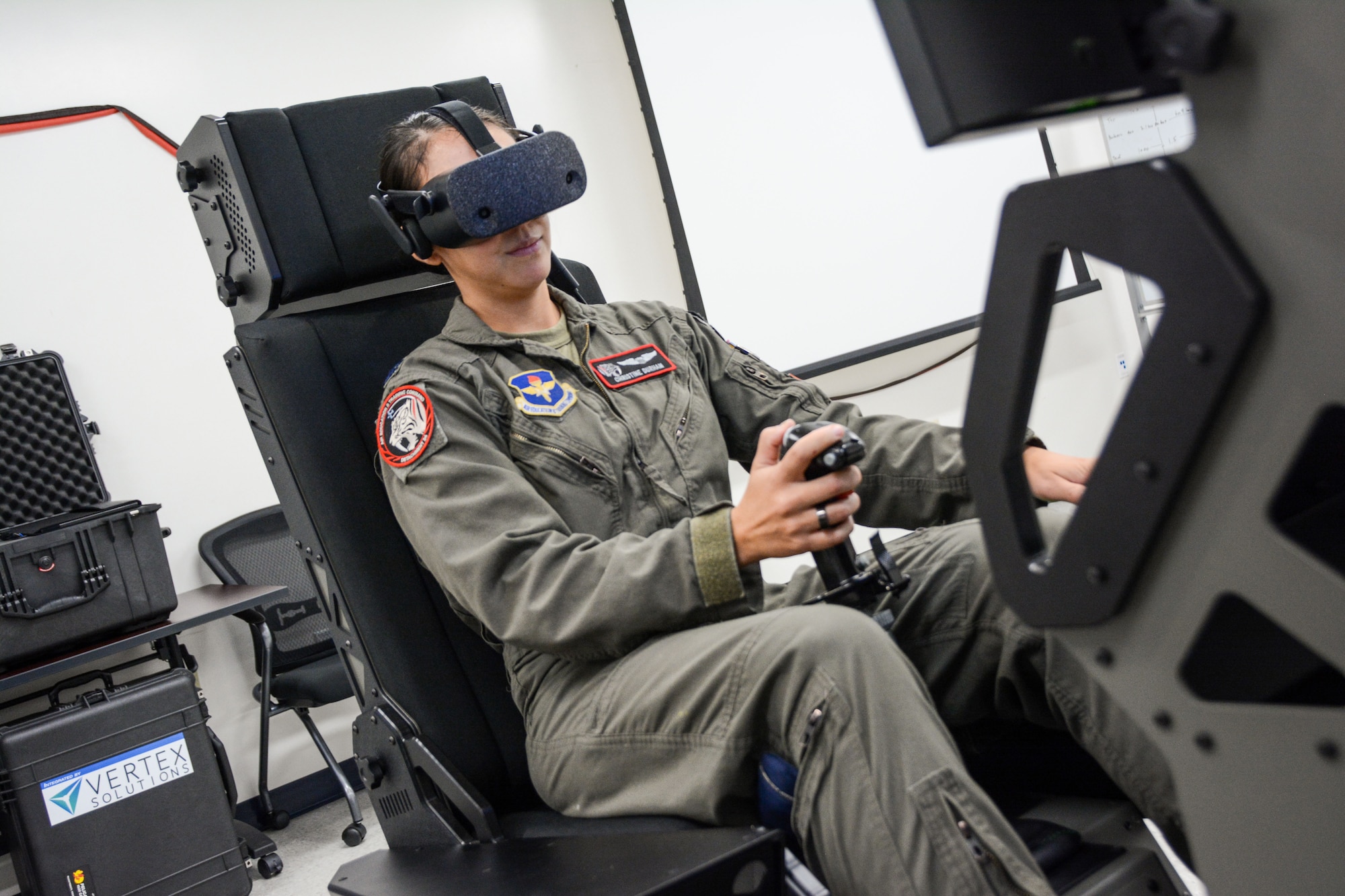 A woman in a military flight suit operates an aircraft simulator.