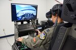 A man in a military flight suit operates an aircraft simulator.