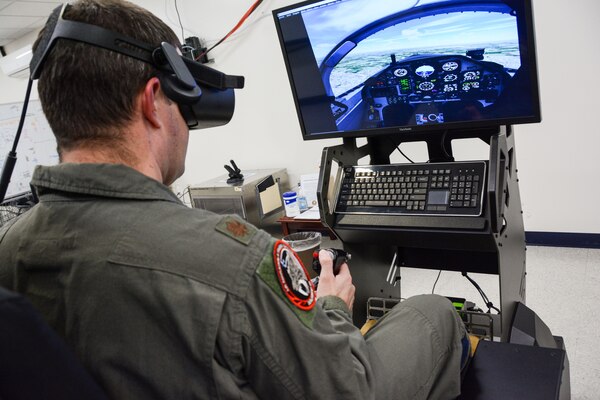 A man in a military flight suit operates an aircraft simulator.