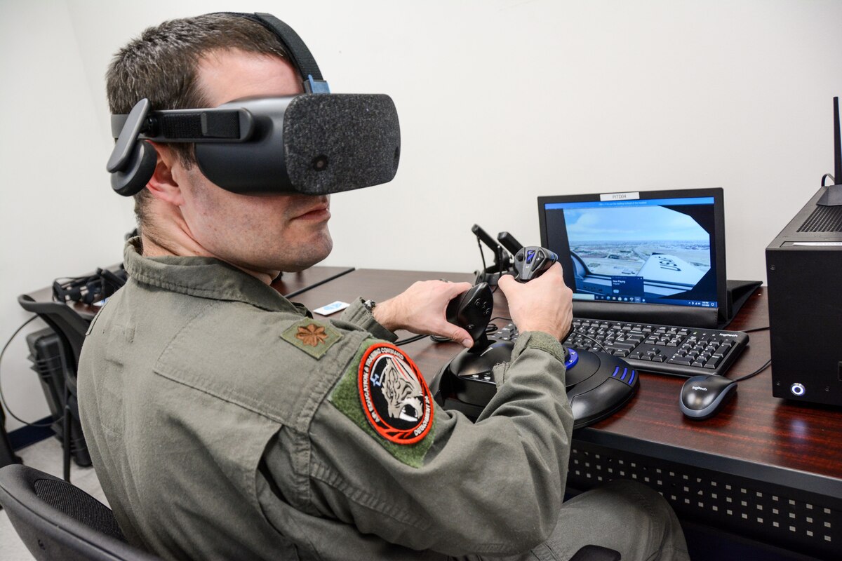 A man in a military flight suit operates an aircraft simulator.
