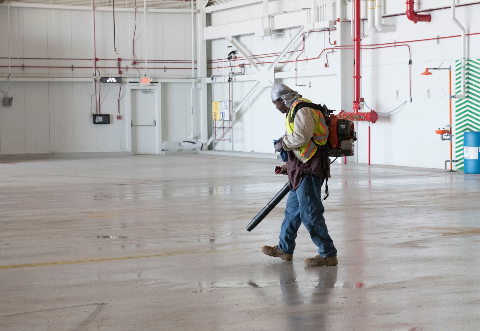 Photo of a man walking with a leaf blower drying a hangar floor