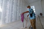 A man places a lei on a metal pole while standing in a room with names carved on the wall.