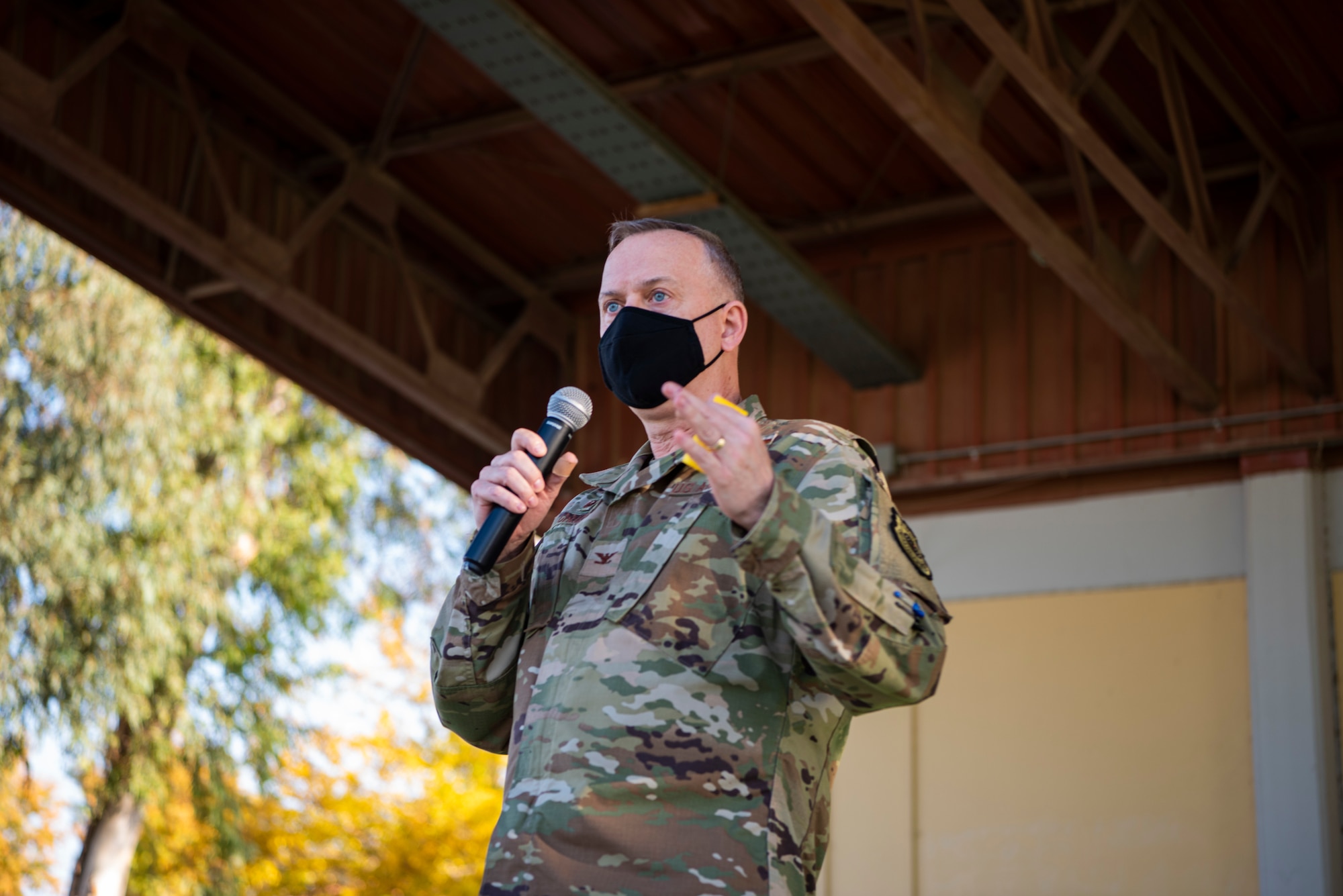 Photo of wing commander holding a microphone and speaking while wearing a mask.