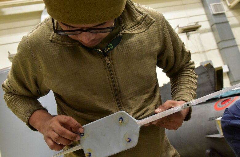An Airman checks screws on a fuel tank part.