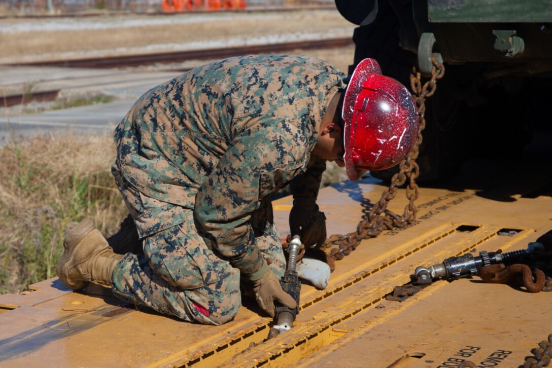 U.S. Marine Corps Lance Cpl. Nicolas Barajas, an embark specialist, 2nd Marine Regiment, 2nd Marine Division, secures chains on a flat railcar on Camp Lejeune, Dec. 2, 2020. Marines rehearsed loading military vehicles onto flat railcars to hone skills and proficiency of railroad operations. Applying railroad knowledge in the Marine Corps allows for a dependable, expedited and cost effective transportation compared to water or air way movement of supplies. (Marine Corps photo by Lance Cpl. Sarah Hediger)