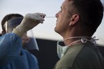 A man leans his head back as he receives a nasal swap from another man in personal protective equipment.