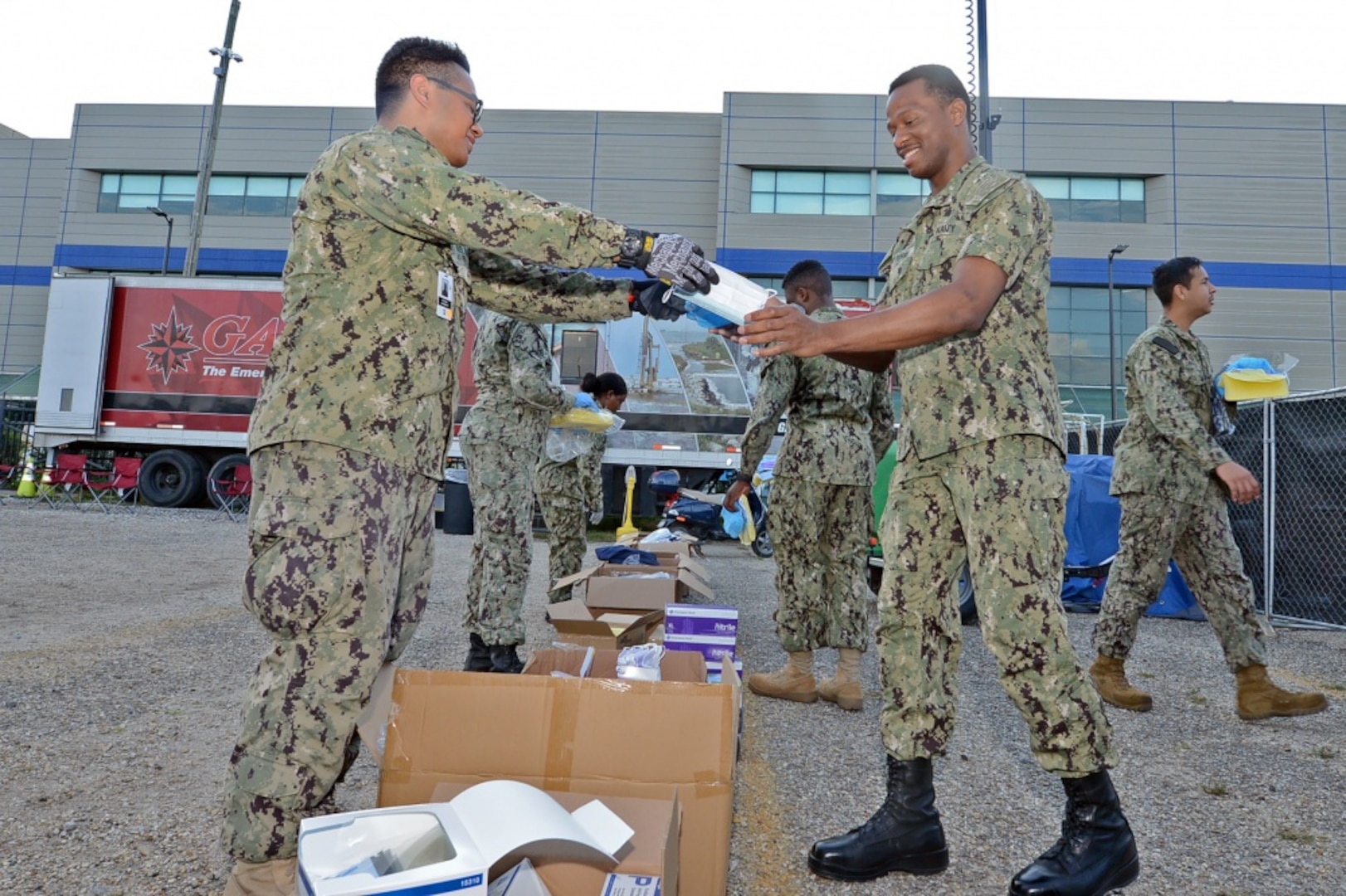 Sailors in Navy warfare uniforms receive packages of personal protective equipment in a line.