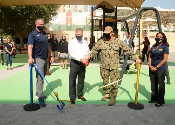 Assistant Secretary of the Navy (Energy, Installations and Environment) Charles Williams, Jr., cuts a ribbon marking the opening of a new playground onboard Naval Support Activity Bahrain with Capt. Greg Smith, commanding officer, NSA Bahrain, Donald Wells, director of morale, welfare and recreation (MWR) Bahrain, and MWR personnel during a tour of Naval Support Activity (NSA) Bahrain.
