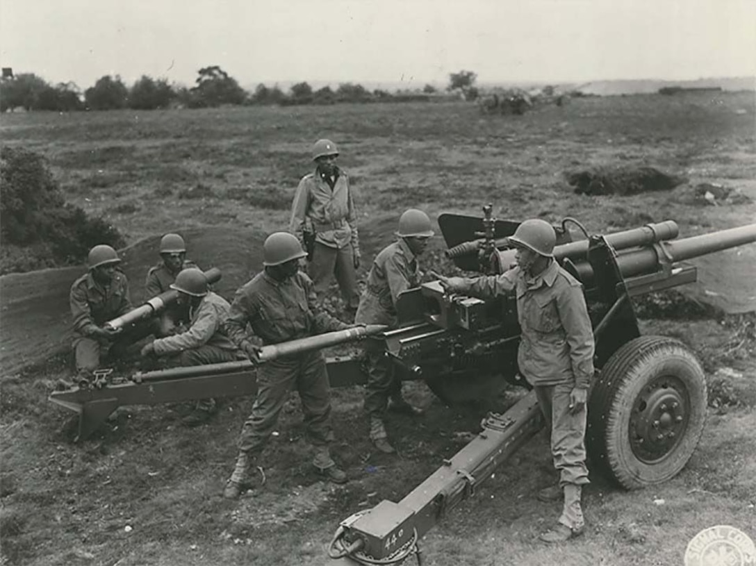 Seven men stand around a field artillery station.