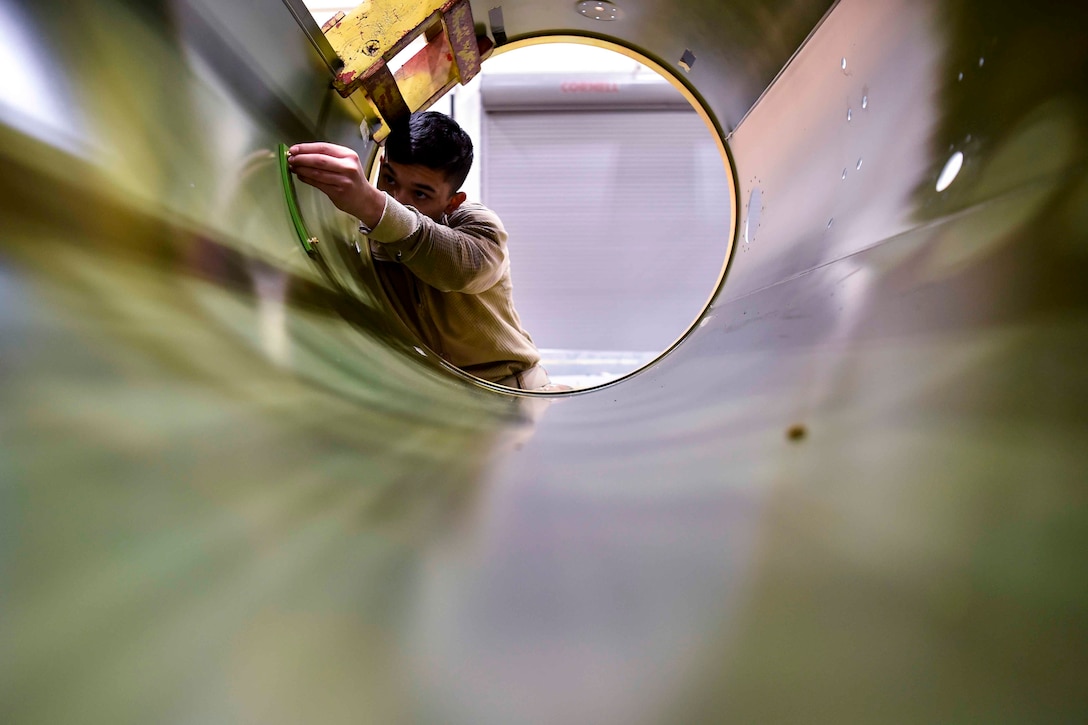 An airman works on the inside of a fuel tank.