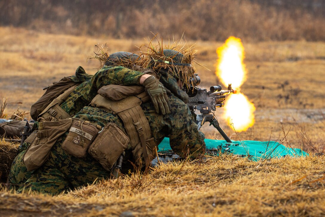 Two Marines fire a weapon in a field.