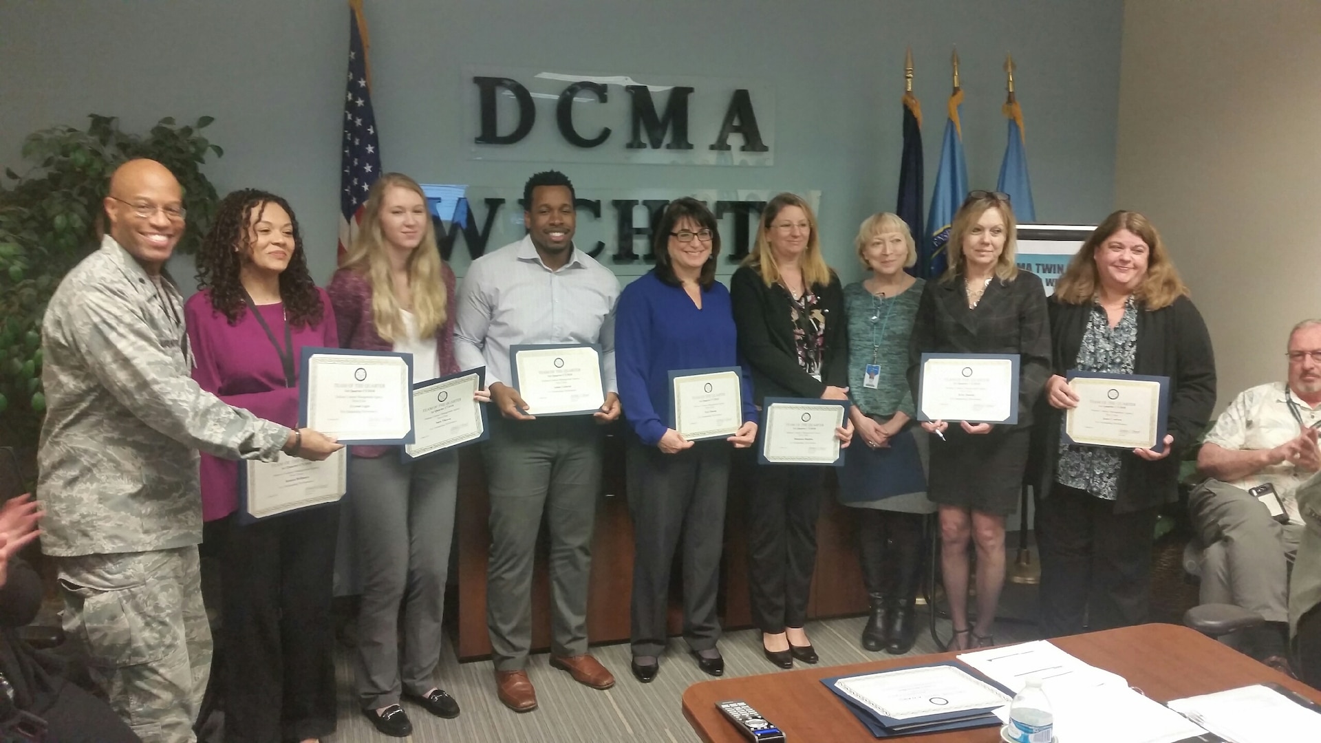 Ten people hold certificates standing in front of a D C M A Wichita sign.
