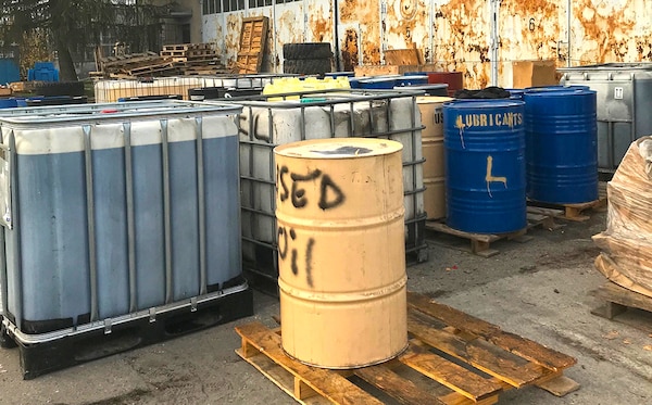 Barrels of fluids sit in a parking lot.