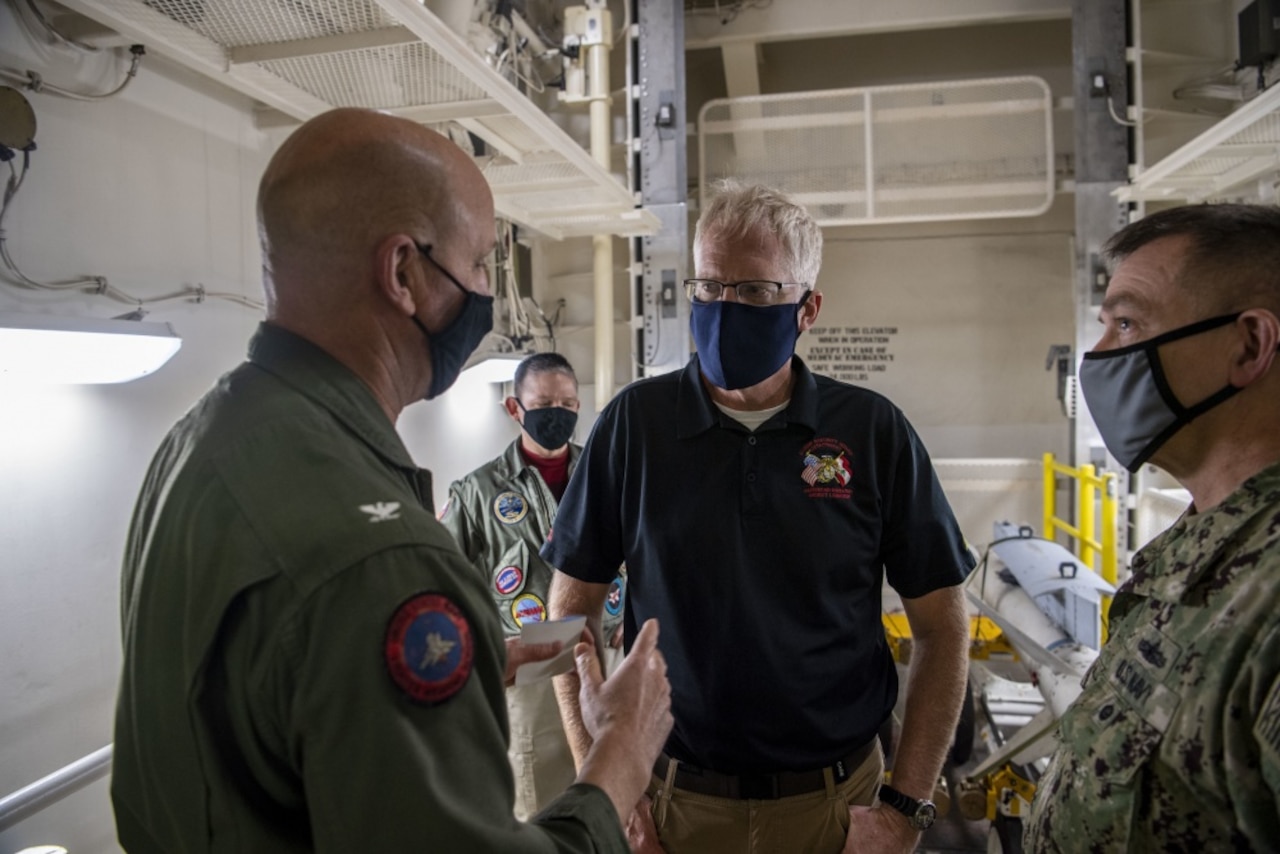 Three men on a ship talk while a fourth man stands in the background.