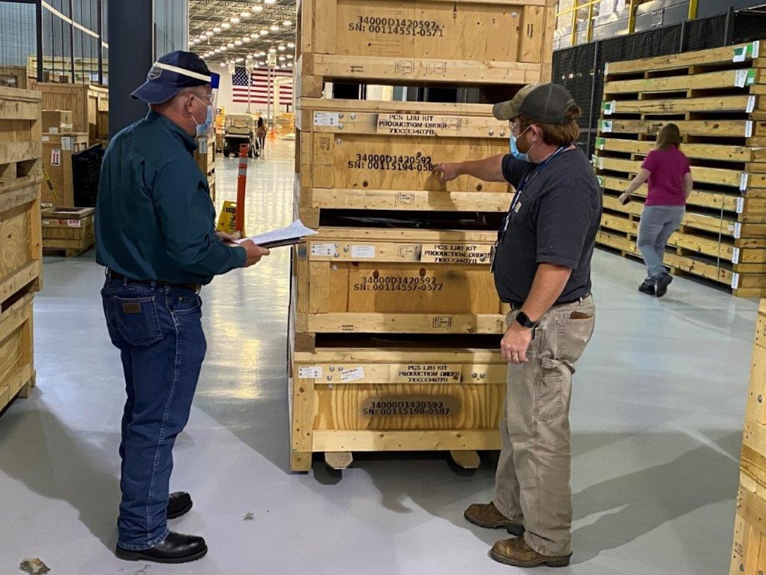 Two men stand in front of pallets and discuss paperwork