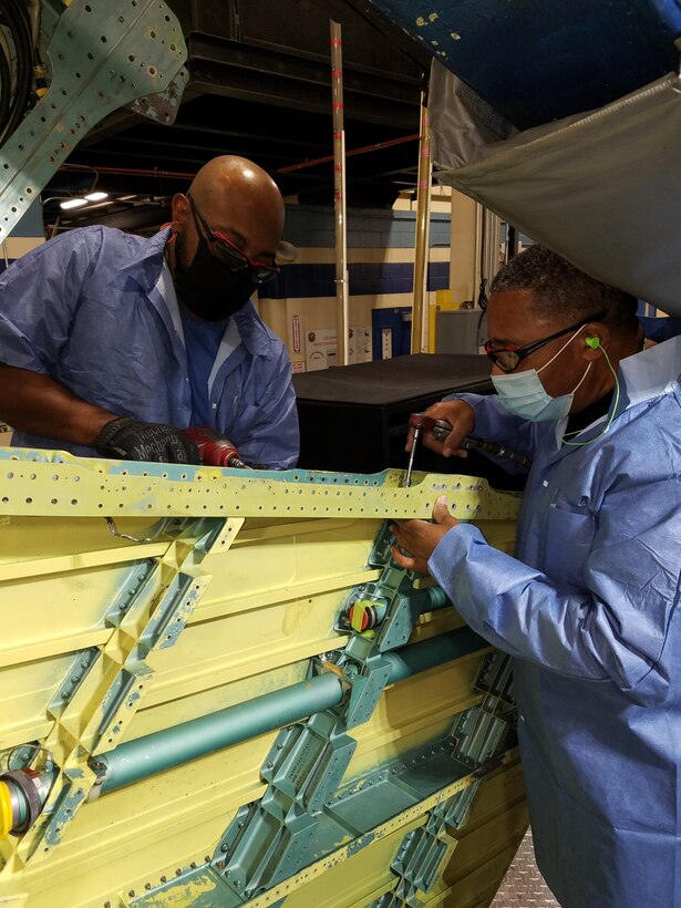 Photo shows two individuals working on an aircraft