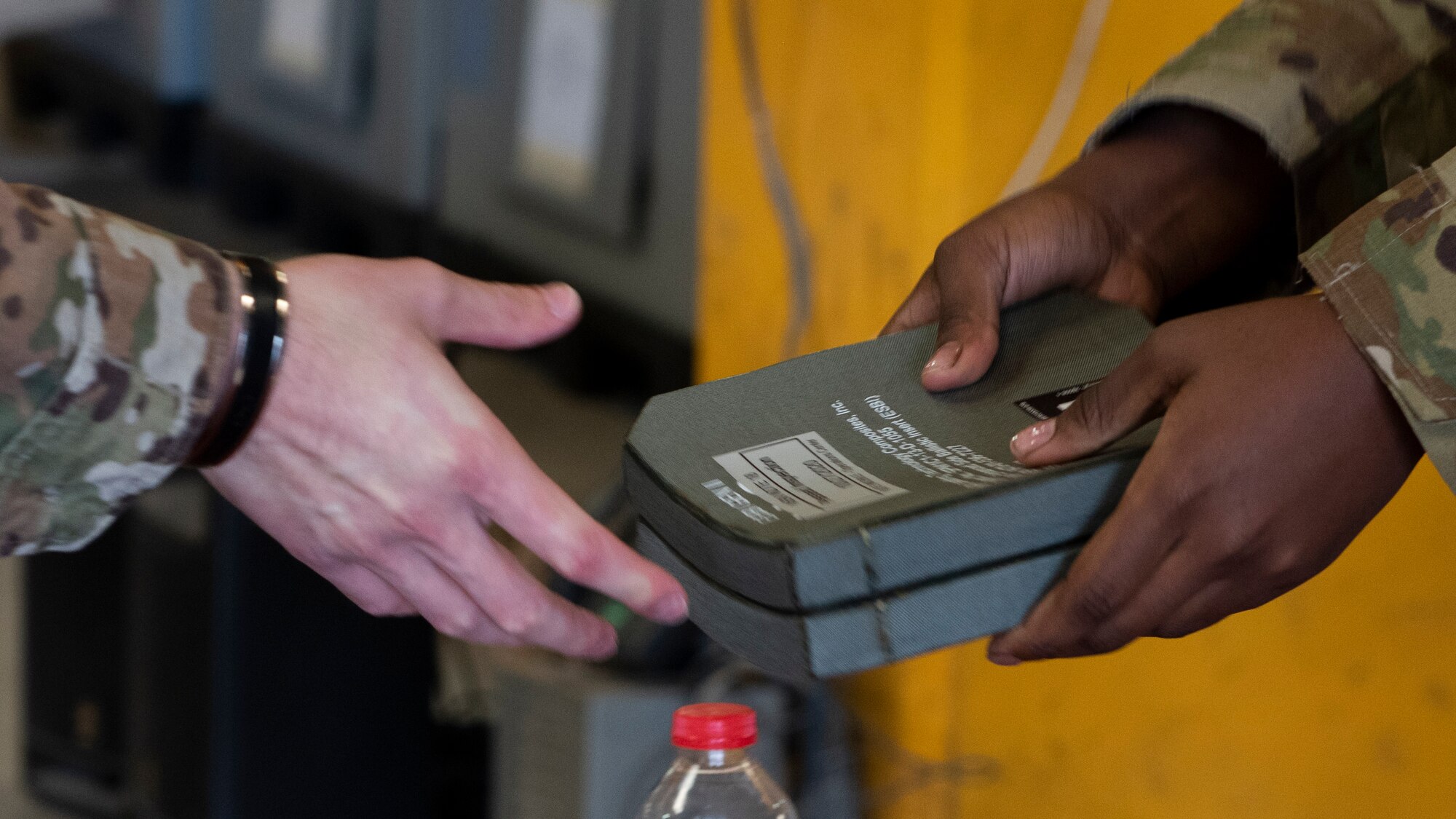 close-up of an Airman handing over two small armor plates to another Airman.