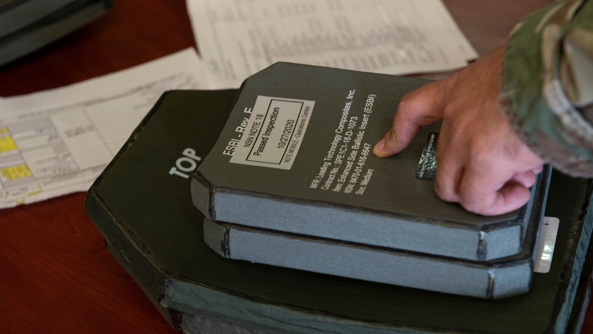 A stack of armor plates on a table is checked by a Airman.