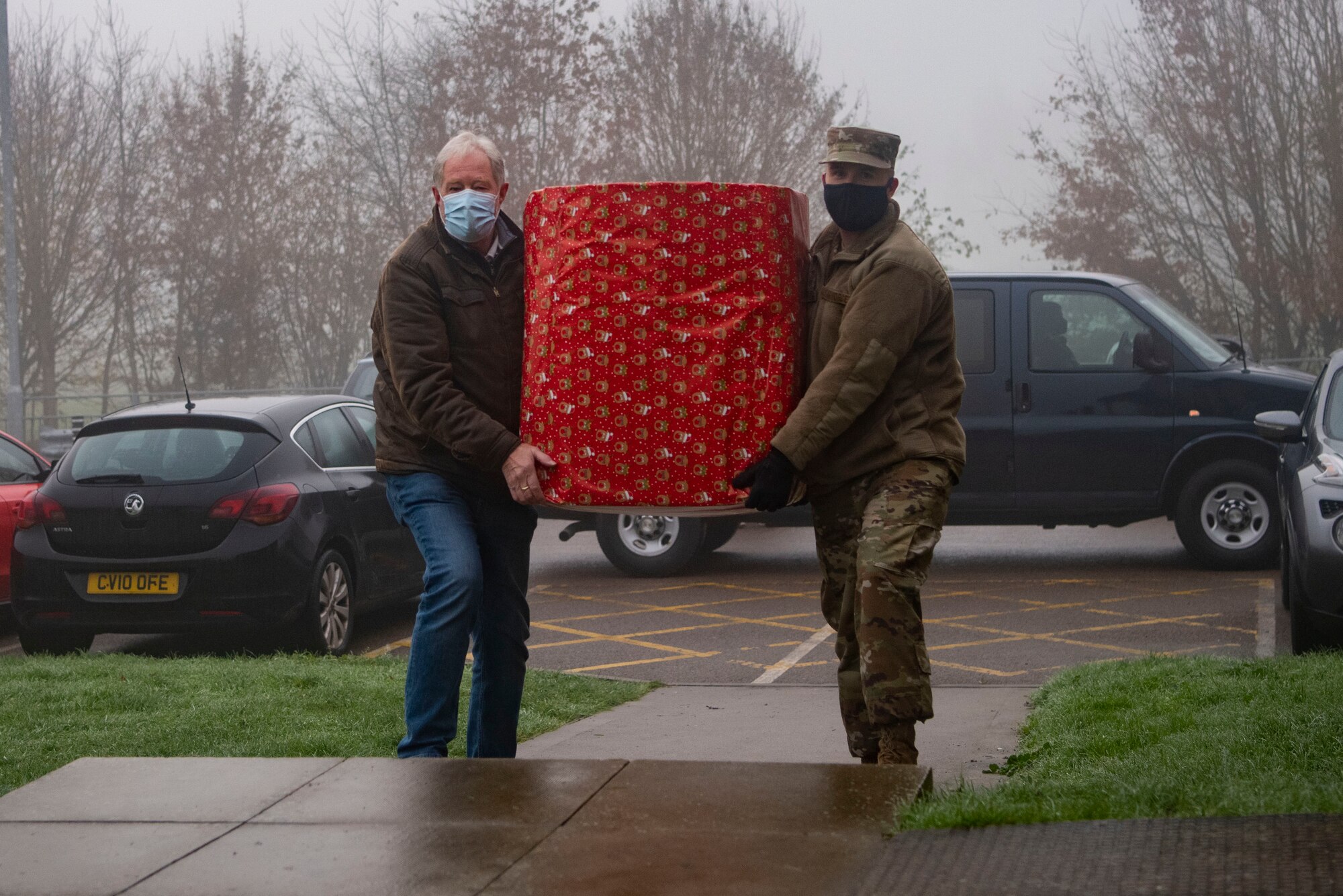 U.S. Air Force Master Sgt. Garrett Hetzel, 95th Reconnaissance Squadron first sergeant, right, and a volunteer carry a box of toys into a local community center in Mildenhall, England, Dec. 7, 2020. Team Mildenhall's first sergeants organized the donation of gifts for families in need in the surrounding community. (U.S. Air Force photo by Airman 1st Class Joseph Barron)
