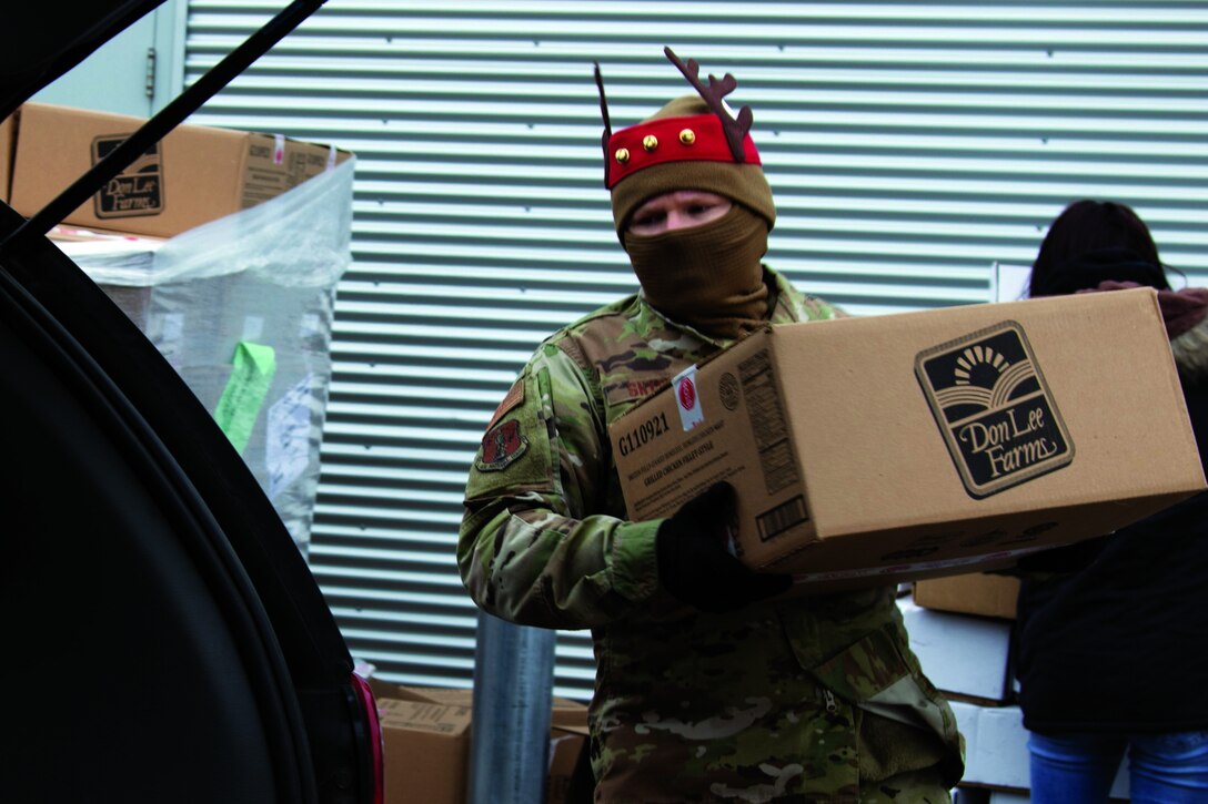 An airman wearing a face mask and gloves carries a box to a vehicle.