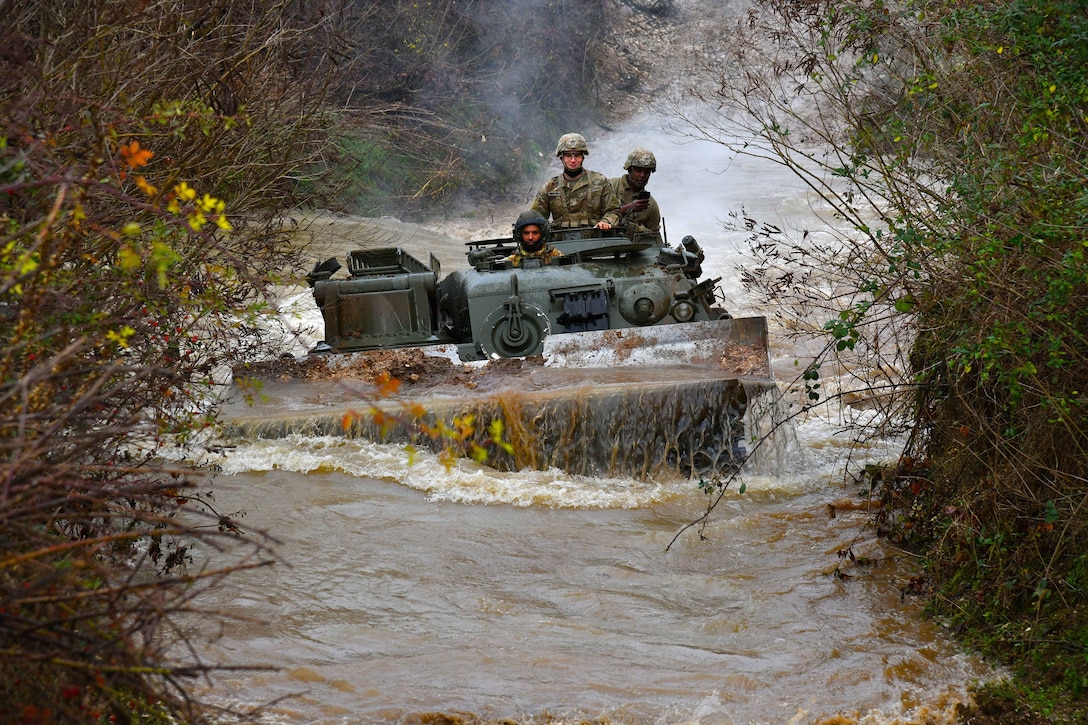 U.S. and Italian troops operate a vehicle through water in the woods.