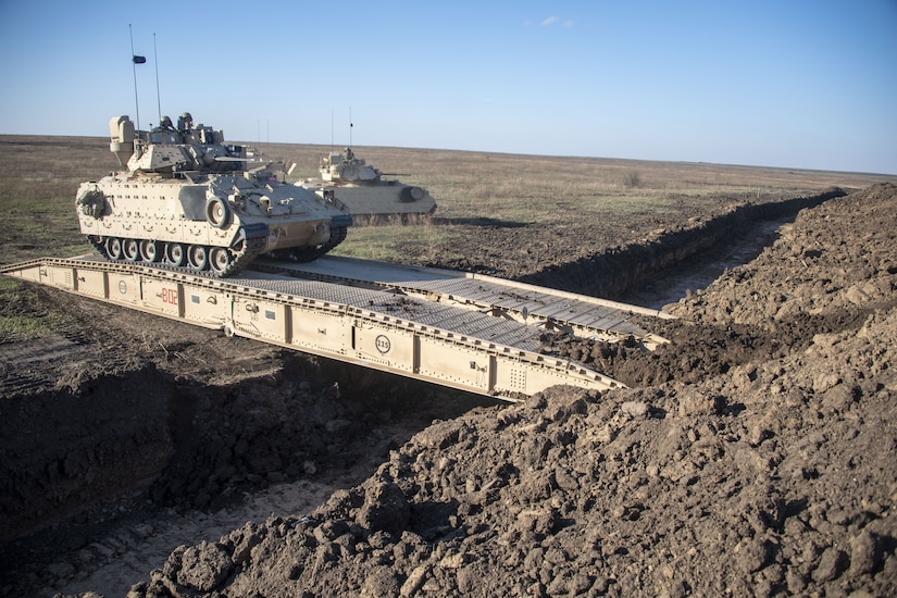A military vehicle crosses a small bridge.