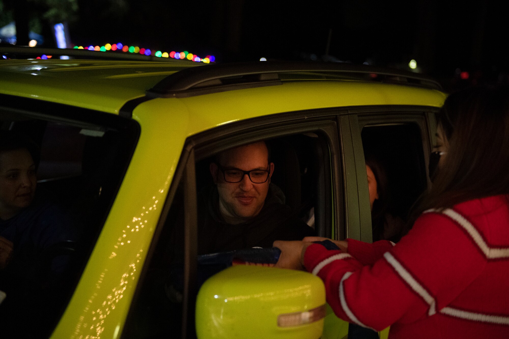 A photo of Maria Galvez, 23d Force Support Squadron digital media specialist, handing a gingerbread house kit to a family during a drive-through holiday dinner.