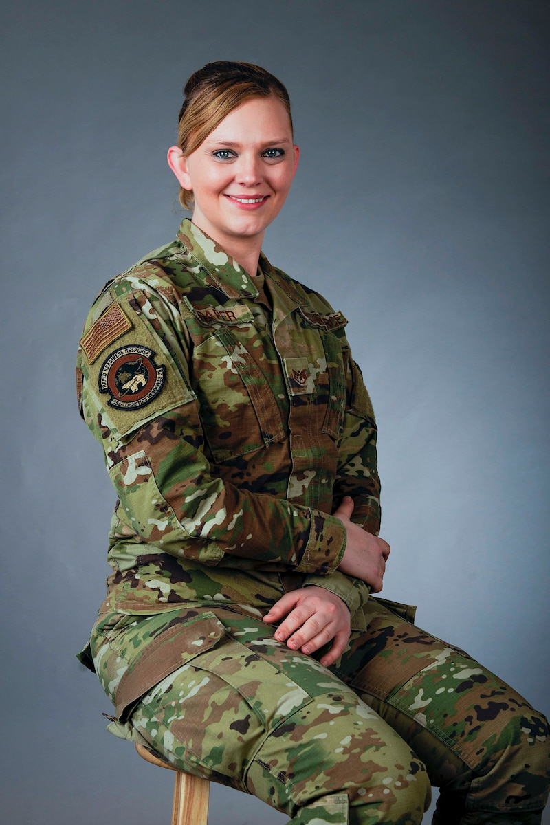 A female Airman sits on a stool looking at the camera smiling.