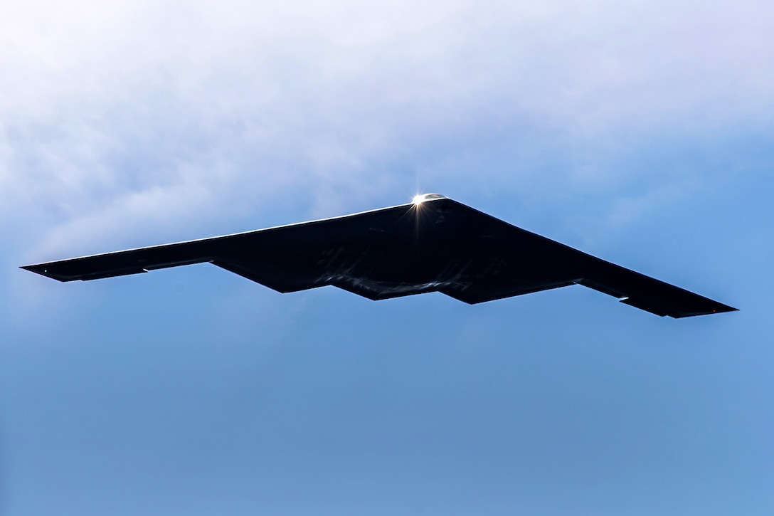 A B-2 Spirit stealth bomber flies in a blue sky.
