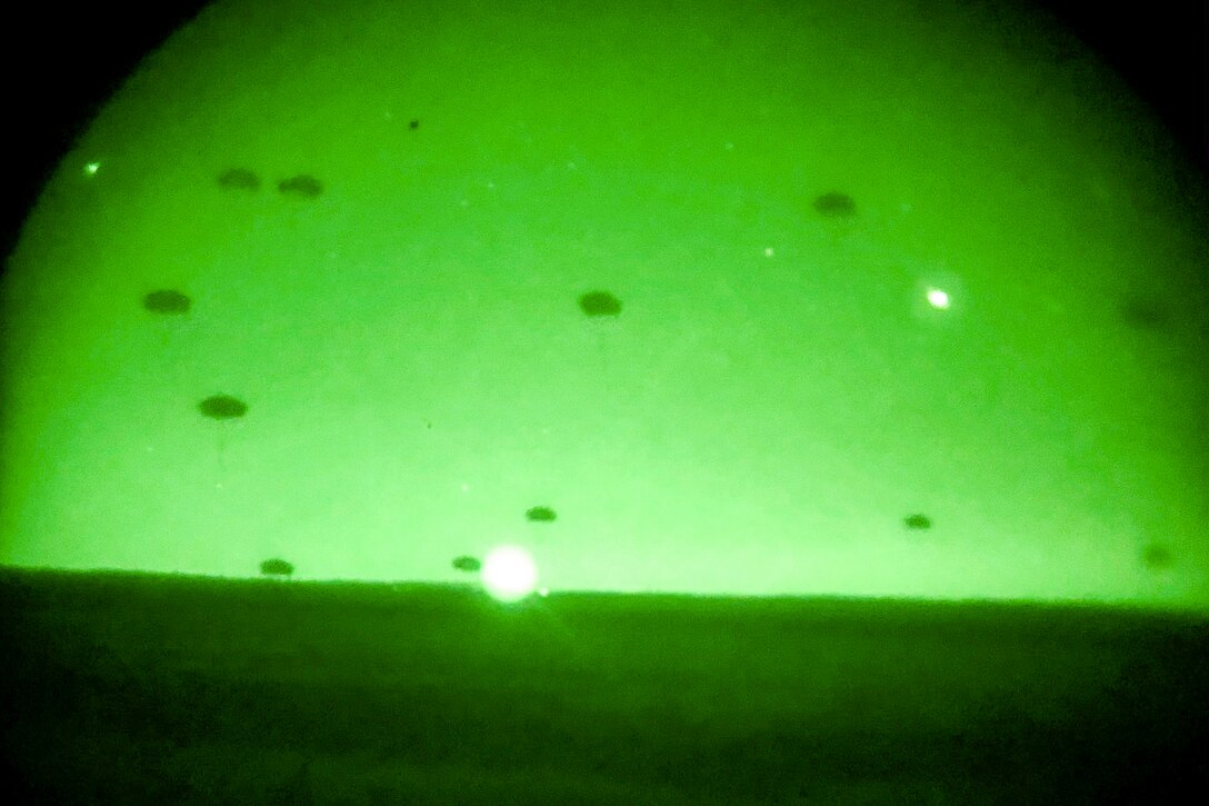 Soldiers  seen through green night vision lens freefall with parachutes.