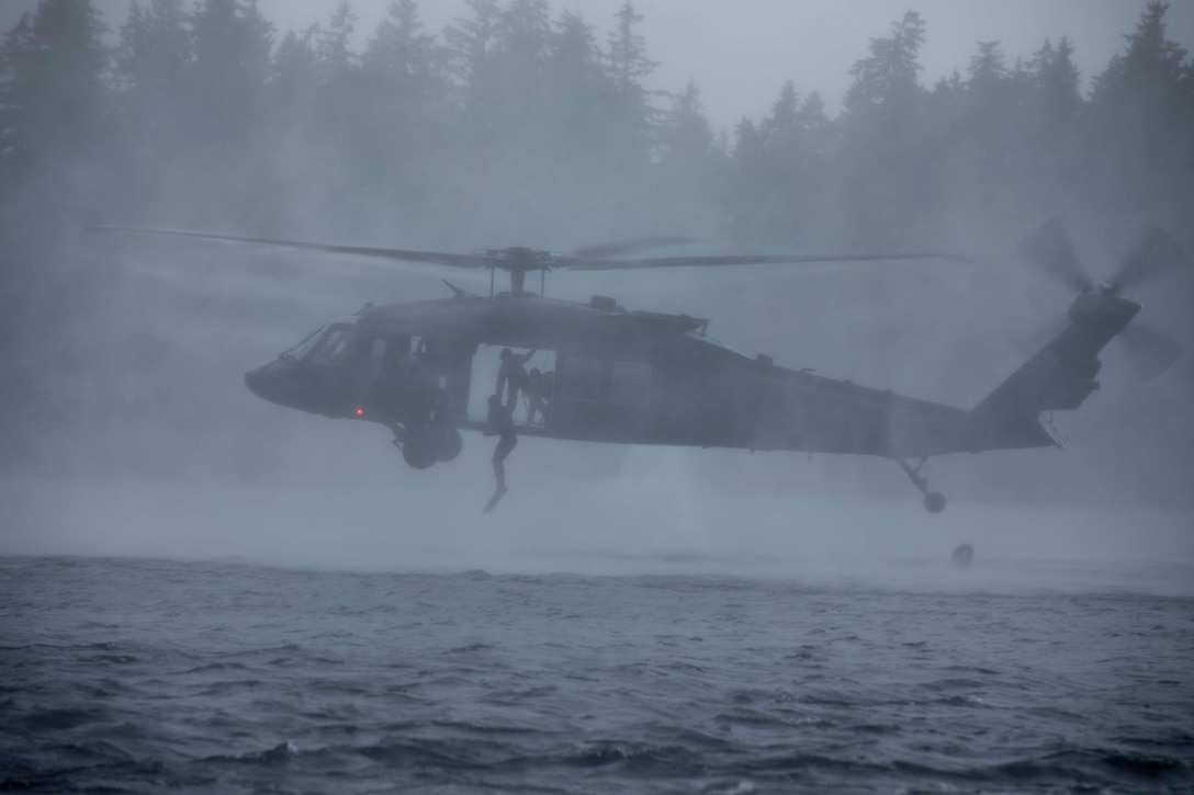 Soldiers jump from a helicopter into water.