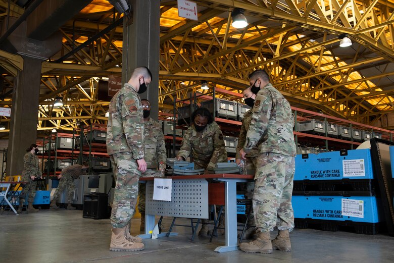 Four Airmen exchange armor plates in an equipment warehouse.