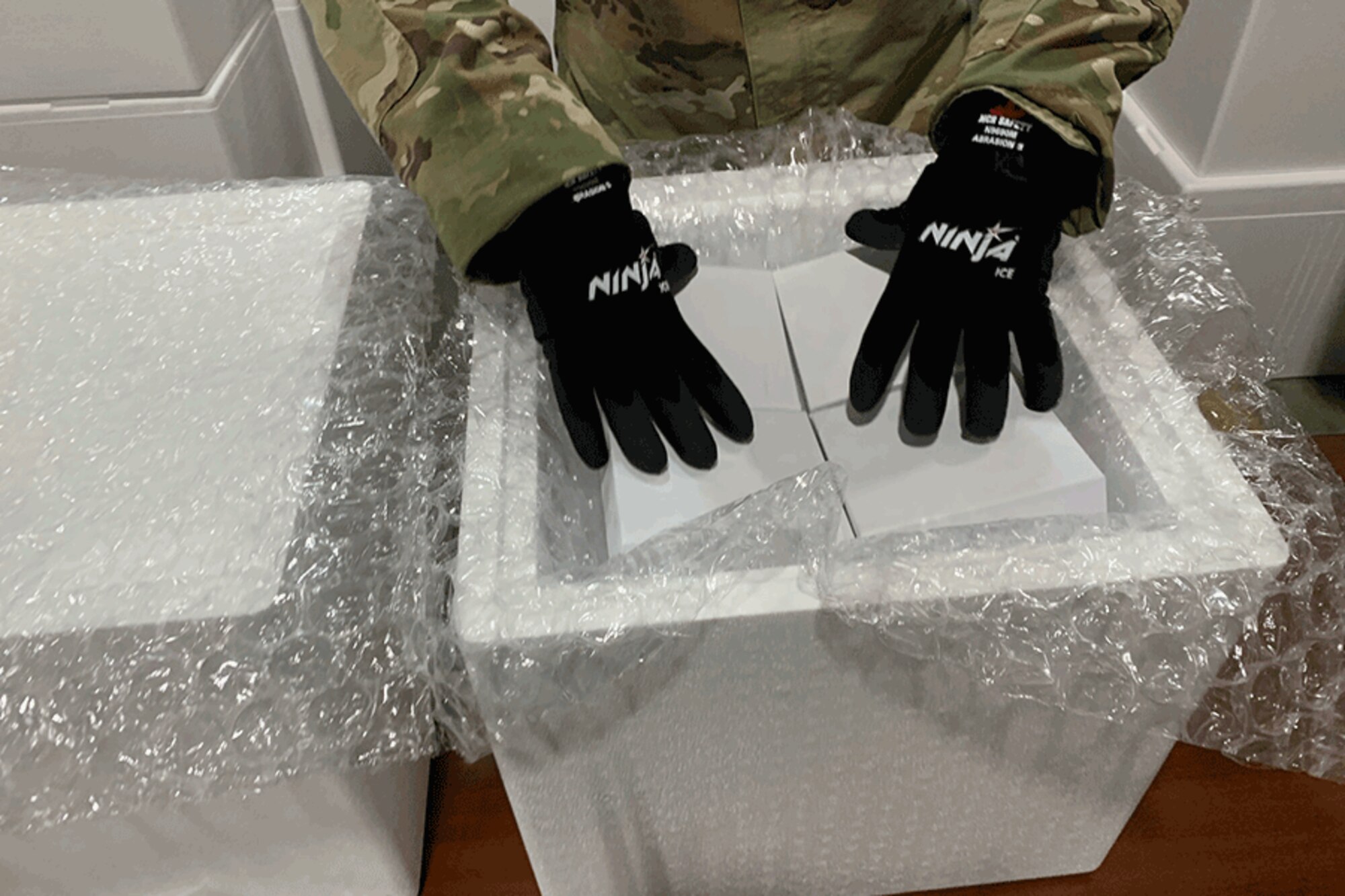 A service member wears gloves as he packs glass vials in ice.