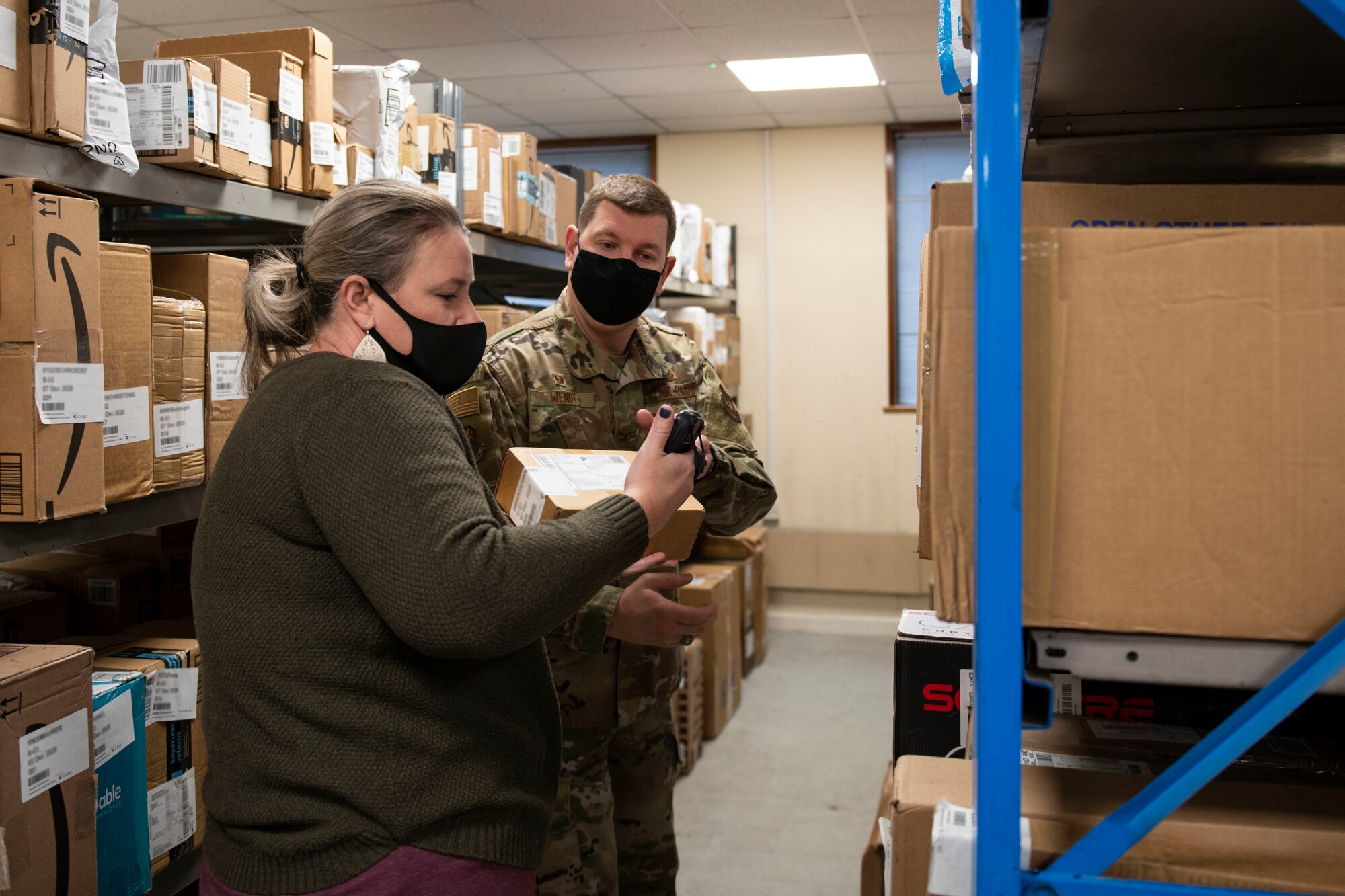 A volunteer shows U.S. Air Force Col. Kurt Wendt, right, 501st Combat Support Wing commander, how to scan packages at the Royal Air Force Molesworth Post Office, England, Dec. 9, 2020. Airmen and civilians have volunteered at the post office to help with the influx of packages during the holiday season. (U.S. Air Force photo by Senior Airman Jennifer Zima)
