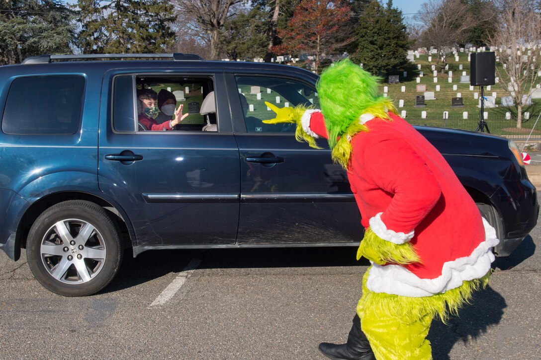 A man dressed as the Grinch waves to two boys in the back seat of an SUV.