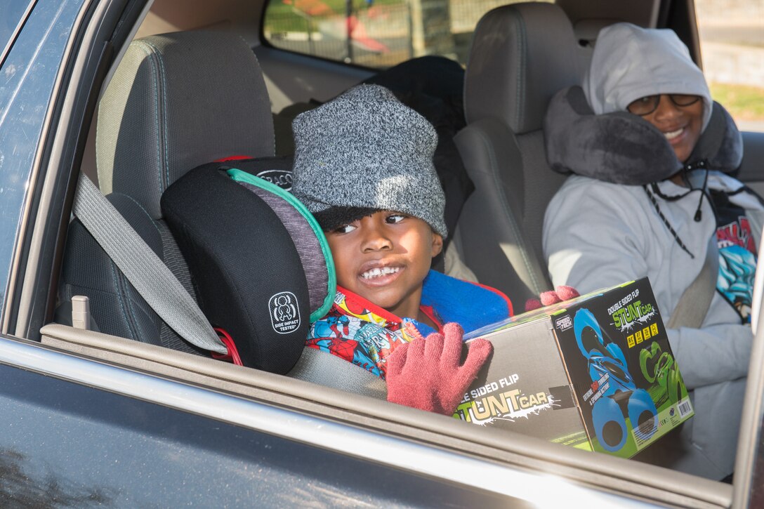 A small child sits in a car holding a box while a woman smiles beside him.