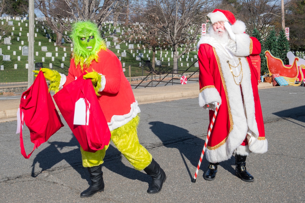 A man dressed as the Grinch slinks away from Santa as he holds two large red bags.