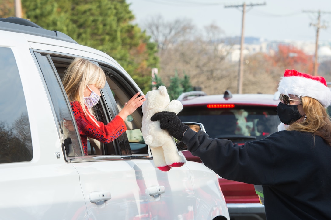 A woman hands a stuffed animal to a child through a car window.