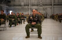 Airmen sit on chairs in a hangar.