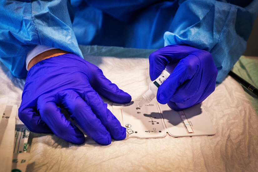 A person wearing personal protective equipment prepares a testing card.