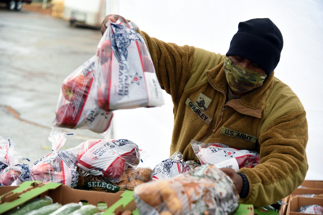 A soldier wearing a face mask delivers boxes of groceries to area residents.