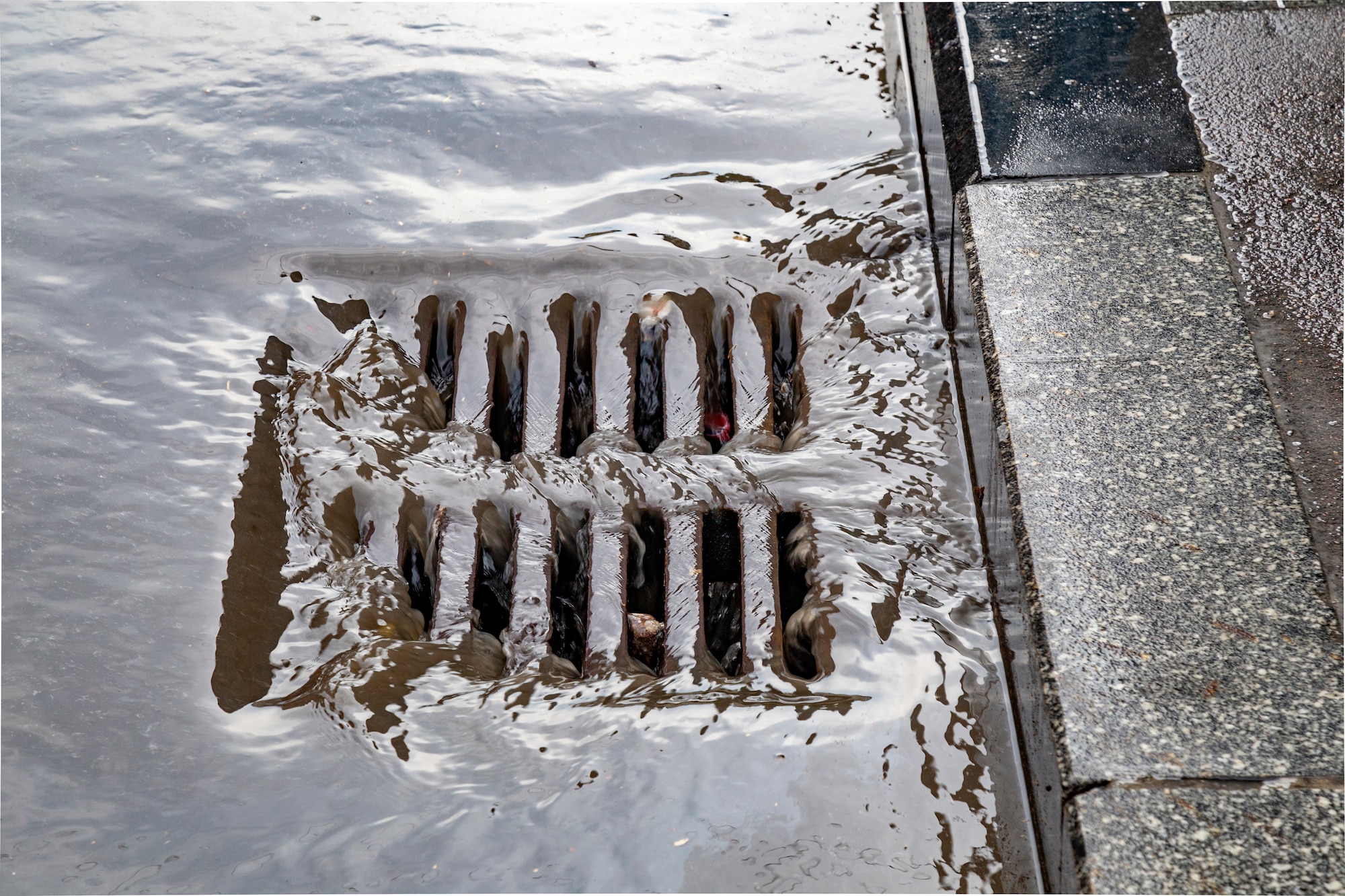 Photo shows water running into a street drain.