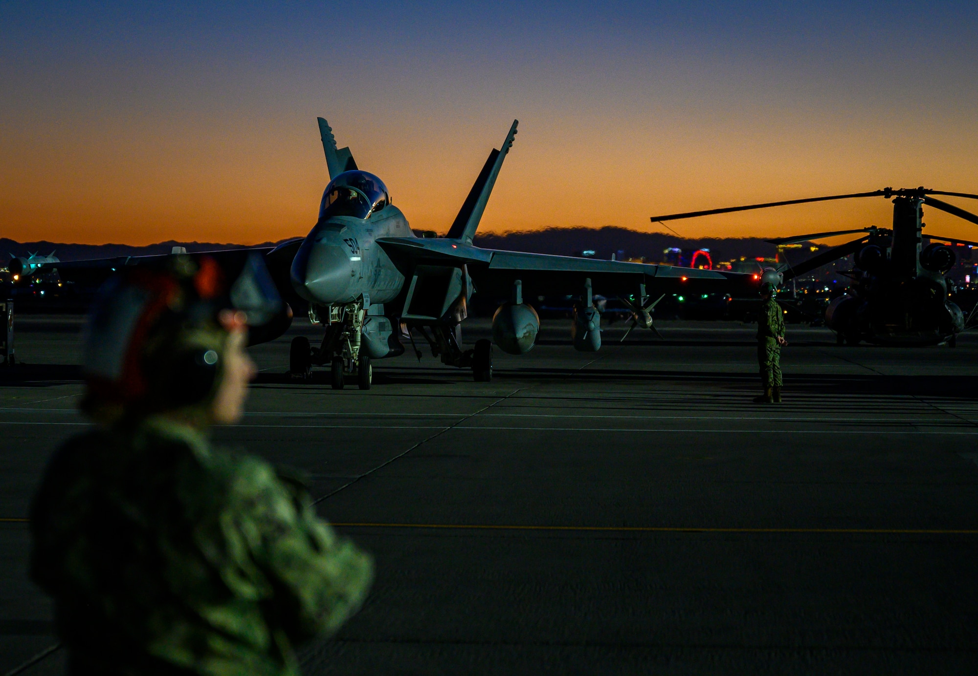 U.S. Navy Airmen stand on the flight line during take-off at night.