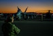 U.S. Navy Airmen stand on the flight line during take-off at night.