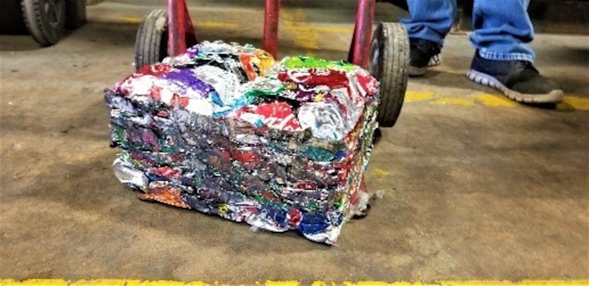 A block of crushed cans sit on a dolly after being crushed at the 97th Air Mobility Wing Recycling Center on Altus Air Force Base, Oklahoma, Dec. 10, 2020. After cans are crushed at the recycling center, they come out in 25-pound blocks for easy transportation. (U.S. Air Force photo by Judy Mott)