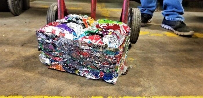 A block of crushed cans sit on a dolly after being crushed at the 97th Air Mobility Wing Recycling Center on Altus Air Force Base, Oklahoma, Dec. 10, 2020. After cans are crushed at the recycling center, they come out in 25-pound blocks for easy transportation. (U.S. Air Force photo by Judy Mott)