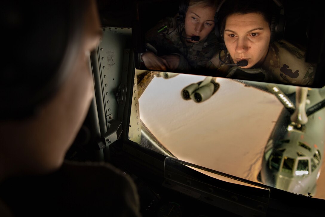 Two service members watch an aircraft refueling as seen through a mirror.