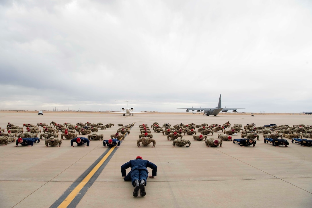 A large group of airmen perform pushups near aircraft.