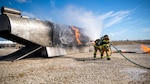 Andrew Sanchez assists Eric Flores, both firefighters with Joint Base San Antonio, during a live fire Aircraft Rescue Fire Fighting training Nov. 20, 2020, at Joint Base San Antonio-Kelly Field, Texas.
