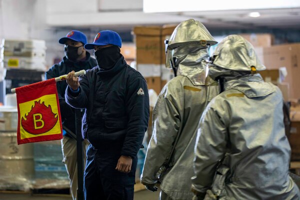 Aviation Boatswain's Mate (Handling) 2nd Class Johnkeith Elopre waves a flag simulating a fuel fire during a fire drill in the hangar bay aboard the Wasp-class amphibious assault ship USS Kearsarge (LHD 3) Dec. 10, 2020.